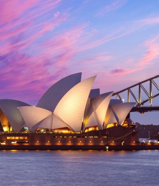 Illuminated Sydney Opera House sails against a vibrant pink sunset sky with the Harbour Bridge behind.