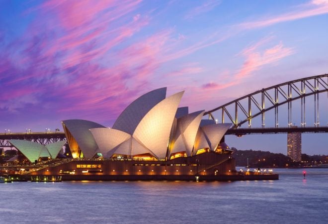 Illuminated Sydney Opera House sails against a vibrant pink sunset sky with the Harbour Bridge behind.