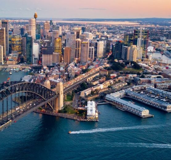 Aerial view of Sydney Harbour Bridge traffic leading into the CBD skyline and Walsh Bay piers at sunset.