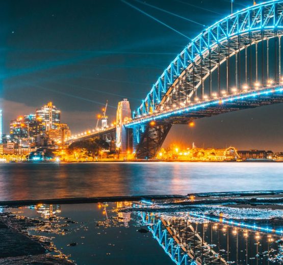 Illuminated Sydney Harbour Bridge and city skyline reflected in the water at night.